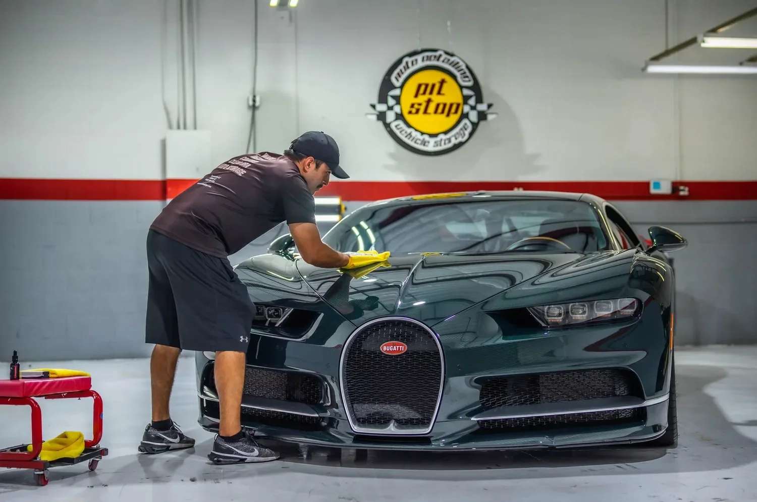 Detailer wiping down a black Bugatti under the Pit Stop shop sign