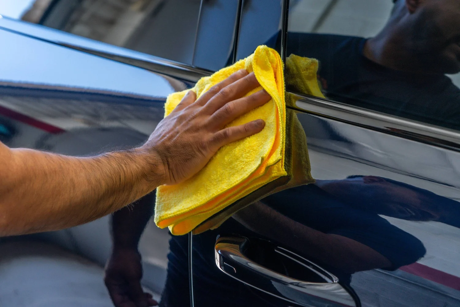 Detailer buffing a coated black door panel with a yellow microfiber cloth